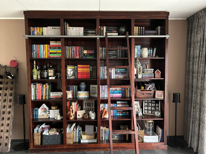 De stoere boekenkast met ladder is gevuld met boeken en decoraties